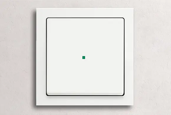 Een witte, aan de muur gemonteerde elektrische schakelaar met een kleine groene indicator in het midden tegen een lichtgekleurde gestructureerde muur.